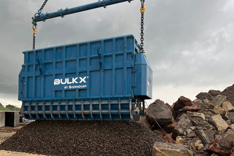 A large blue skip with BulkX by Conquip on the side dropping large quantities of soil.